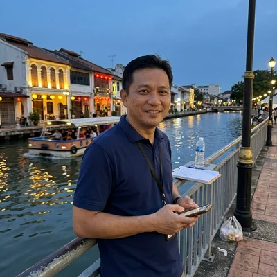 Gana, tour operations lead at Malacca Tours, by the illuminated Malacca River at dusk
