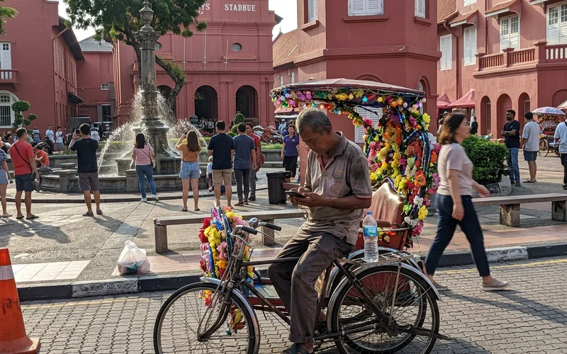 A decorated trishaw and visitors outside the red Stadthuys at Dutch Square