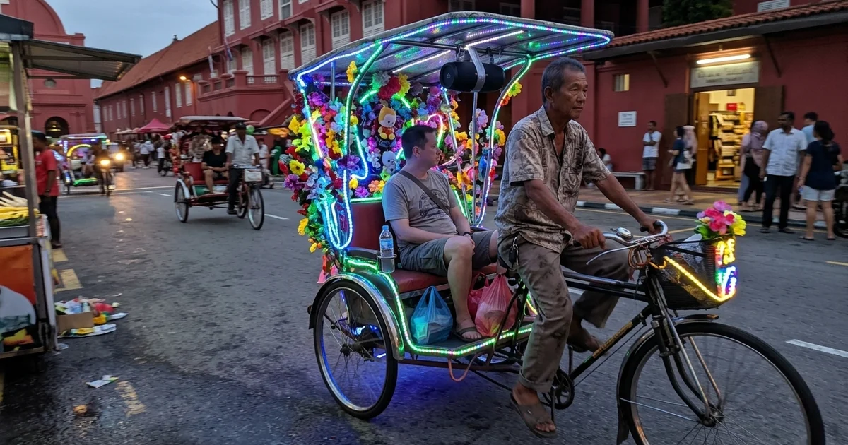 A brightly decorated neon trishaw carrying a passenger near Dutch Square in Malacca at dusk
