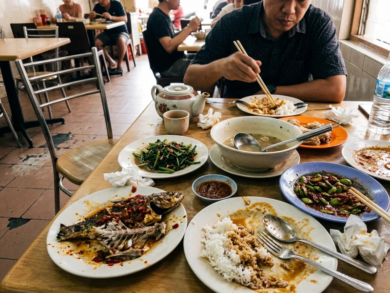 A table of local Malacca dishes mid-meal under warm restaurant light