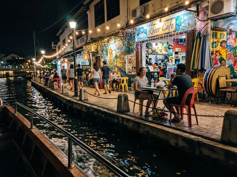 Lit riverside murals and cafes seen from the water after dark